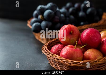 Rote und frische Pflaumen mit Trauben in einem Korb auf Ein schwarzer Tisch Stockfoto