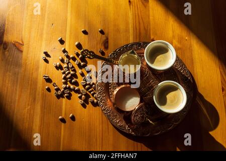 Türkischer Kaffee in Kupferbecher und -Topf serviert.Kaffeebohnen auf braunem Holztisch. Stockfoto