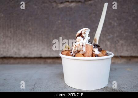 Close - Up Outdoor view at White Frozen Yoghurt Serve with Belag with Melone, Kiwi and chocolate in paper white Cup, on the floor. Stockfoto