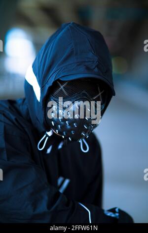 Schwarze Maske mit Nieten auf schwarzem Kapuzenpulli gekleideten Mann Stockfoto