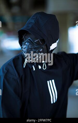 Schwarze Maske mit Nieten auf schwarzem Kapuzenpulli gekleideten Mann Stockfoto