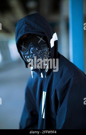 Schwarze Maske mit Nieten auf schwarzem Kapuzenpulli gekleideten Mann Stockfoto