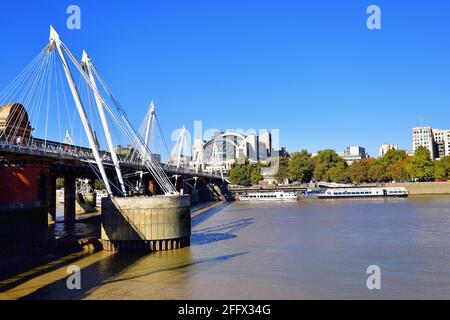 London, England, Vereinigtes Königreich. An den Piers entlang des Uferdamms festsitzende Boote sitzen an der Themse neben der Golden Jubilee Bridge. Stockfoto