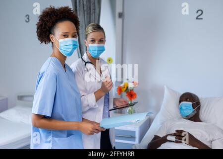 Porträt zweier verschiedener Ärztinnen mit Gesichtsmasken im Stehen Neben dem männlichen Patienten Stockfoto