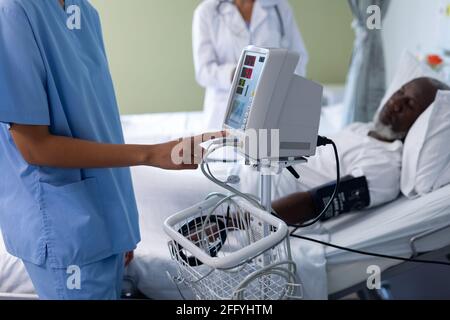 Mittelteil einer Ärztin mit gemischter Rasse, die einen Blutdruck-Monitor verwendet Im Patientenzimmer Stockfoto