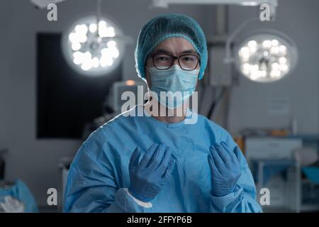 Porträt eines asiatischen Chirurgen mit Gesichtsmaske, Handschuhen, Mütze und Peelings im Operationssaal Stockfoto