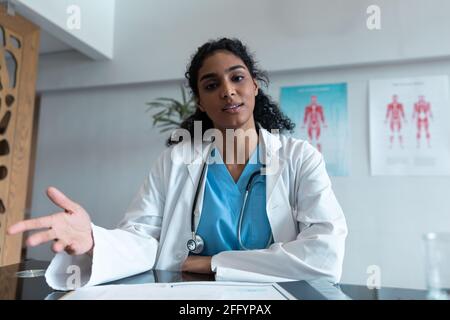 Mixed Race weibliche Ärztin am Schreibtisch reden und gestikulieren während Videokonferenz Stockfoto