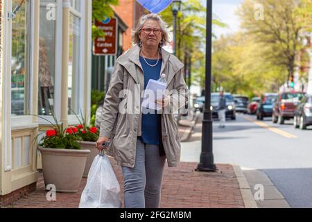 Easton, MD, USA 04-16-2021: Eine blonde ältere Frau trägt einen vollen Beutel mit Müll in schweren weißen Mülltüten mit gequetschter Oberseite und Griff. Müll Stockfoto