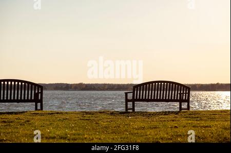 Isolierte Holzbänke am Wasser mit Blick auf einen ruhigen Fluss bei Sonnenuntergang. Abstraktes, vielseitiges Bild mit Kopierbereich. Entspannend, Freizeit, ruhige CO Stockfoto