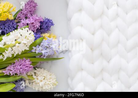 Bouquet von frühlingshaften Blüten von Hyazinthen. Weißer Marmorhintergrund und flauschiges Strickmuster Stockfoto