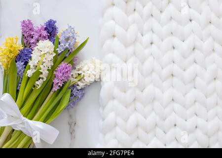 Bouquet von frühlingshaften Blüten von Hyazinthen. Weißer Marmorhintergrund und flauschiges Strickmuster Stockfoto