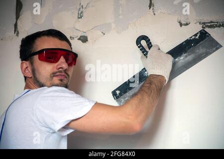 Arbeiten Sie an der Fertigstellung der Wände mit Mischungen aus Gips und Kitt beim Bau eines Hauses. bauarbeiter Verputzen Fassade des Hochhauses mit Kitt Messer. Nivellierung Steinwände Stockfoto