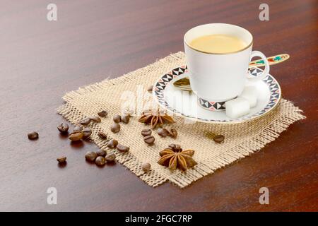 Kaffee in Porzellanbecher mit Untertasse und Kaffeebohnen mit Sternanise. Vintage-Kaffeeset auf Holztisch, mit Zucker und Kaffeebohnen Stockfoto
