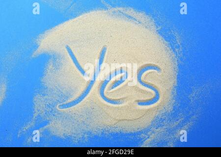 Das Wort ja steht im Sand auf blauem Hintergrund. Stockfoto