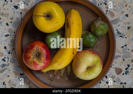 Hausgemachte Stillleben von einem Teller mit saisonalen Früchten, ein köstliches vegetarisches Dessert aus Bananen, Apfel und Pflaumen. Rohe, gesunde und unverarbeitete Lebensmittel, lecker Stockfoto