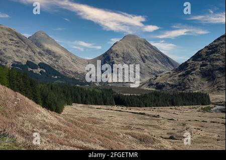 Berge von Glen Etive in den schottischen Highlands an einem sonnigen Tag mit blauem Himmel und leichter Wolke. Tal und Wald vor Bergen. Stockfoto