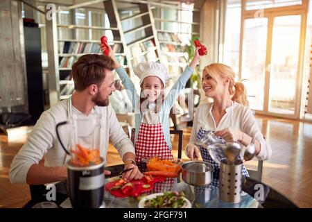 Eine junge Familie ist begeistert, während sie gemeinsam zu Hause in fröhlicher Atmosphäre ein Essen zubereitet. Familie, zusammen, zu Hause Stockfoto