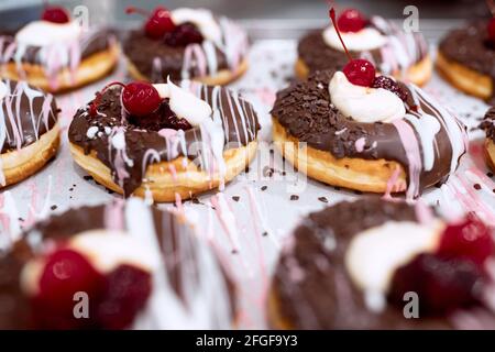 Köstliche Donuts von unwiderstehlichem Aussehen mit Schokoladenüberzug und Kirsche auf der Oberseite auf dem Tablett bereit für eine Konditorei. Gebäck, Dessert, süß Stockfoto