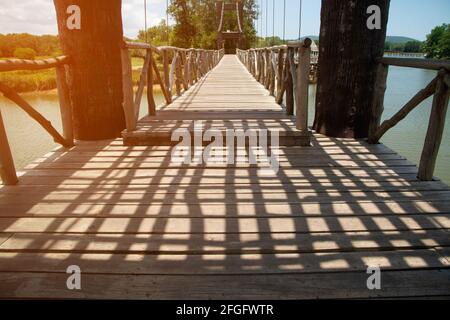 Dunkler Schatten am Tag auf einer hölzernen Hängebrücke, die einen Stausee in einem Park in Thailand überquert. Stockfoto