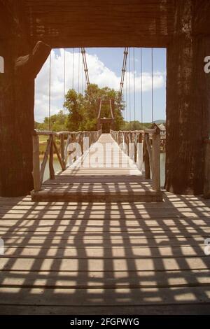 Dunkler Schatten am Tag auf einer hölzernen Hängebrücke, die einen Stausee in einem Park in Thailand überquert. Stockfoto