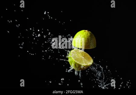 Saft spritzt aus einer geschnittenen Limette auf schwarzem Hintergrund. Stockfoto