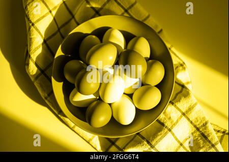 Hühnereier in einem Teller auf einem karierten Küchentuch. Konzept der landwirtschaftlichen Produkte und natürliche Ernährung. Hartes Sonnenlicht und Schatten. Getönte in Beleuchtung und Stockfoto