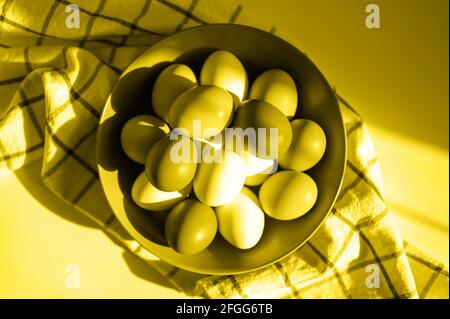 Hühnereier in einem Teller auf einem karierten Küchentuch. Konzept der landwirtschaftlichen Produkte und natürliche Ernährung. Hartes Sonnenlicht und Schatten. Getönte in Beleuchtung und Stockfoto
