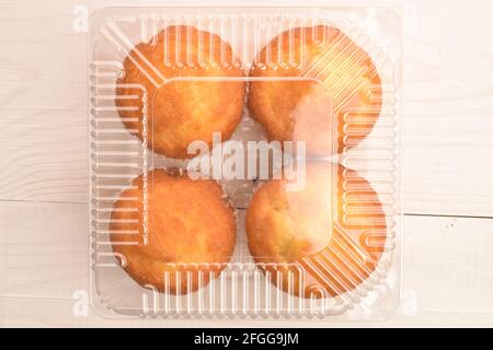 Vier duftende Cupcakes in einer Plastikbox, Nahaufnahme, auf einem Holztisch, Draufsicht. Stockfoto