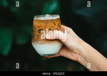Hand halten Eis Latte Kaffee in einem Glas mit Creme auf dem Boden. Kalten Sommer trinken Hintergrund Stockfoto