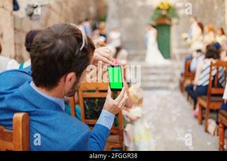 Mann fotografiert eine Hochzeitszeremonie auf einem Smartphone. Leerer Bildschirm Stockfoto