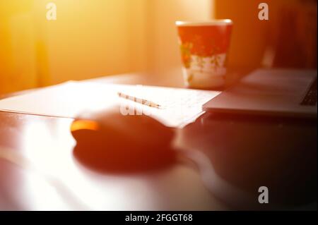 Arbeiten von zu Hause aus. Arbeitsplatz mit Laptop, Computermaus, einer Tasse Tee oder Kaffee und einem Bleistift mit Papier für Notizen. Selektiver Fokus. Fackel Stockfoto