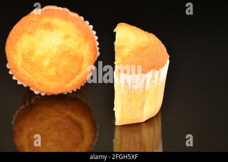 Eineinhalb leckere, schmackhafte Cupcakes aus nächster Nähe vor schwarzem Hintergrund. Stockfoto