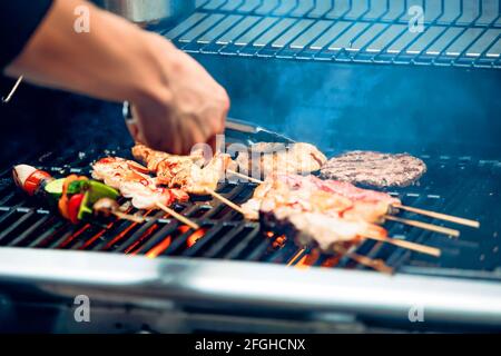 Koch kocht Koteletts für Hamburger, Fleisch-, Hühnchen- und Gemüsespieße auf Grill Stockfoto