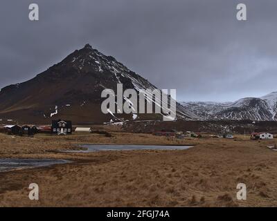 Blick auf das kleine Dorf Arnarstapi, Teil von Snæfellsbær, an der Südküste der Halbinsel Snæfellsnes, Island an bewölktem Wintertag mit gefrorenem See. Stockfoto