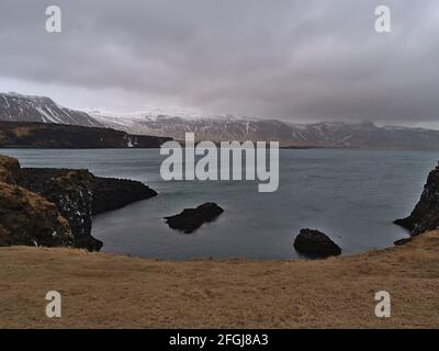 Blick auf die raue Atlantikküste der Halbinsel Snæfellsnes, Westisland bei Arnarstapi im Winter mit brauner Wiese, vulkanischem Basaltgestein. Stockfoto