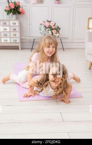 Vertikale Foto von paar kleinen Mädchen spielen auf Yoga-Matte lächeln im Wohnzimmer, gesunde Lebensgewohnheiten und Lifestyle-Konzept. Stockfoto