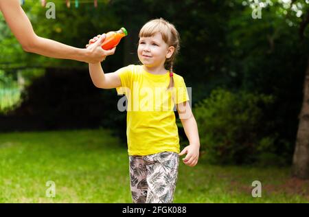 Mutter gab ihrer kleinen Tochter eine Glasflasche voller gesundem Karottensaft, Garten, draußen. Kinderernährung, nahrhafter Gemüsesaft voll o Stockfoto