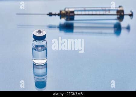 Glas-Impfstofffläschchen und Glasspritze auf blauem Glashintergrund Stockfoto