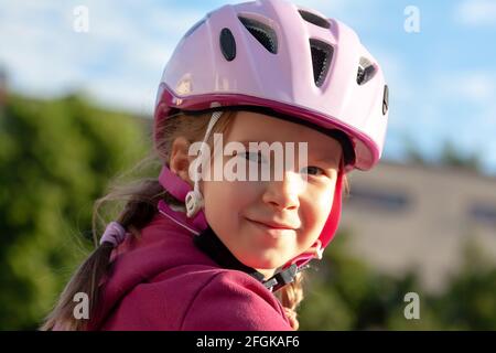 Junge fröhliche Biker-Mädchen, kleine Radfahrer, Kind in einem Schutzhelm auf dem Fahrrad lächelnd, Porträt, Gesicht Nahaufnahme, Blick auf die Kamera, im Freien Stockfoto