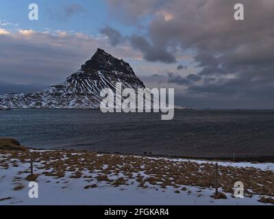 Schöne Aussicht auf den berühmten Berg Kirkjufell an der Nordküste der Halbinsel Snæfellsnes, Island in der Wintersaison mit schneebedeckter Wiese. Stockfoto