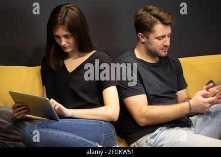 Attraktives Paar mit Smartphone und Tablet chatten online ignorieren ein anderes Stockfoto