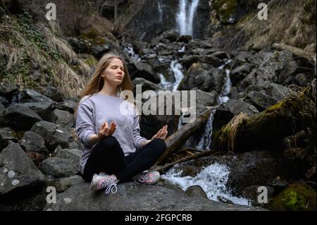 Das Mädchen sitzt auf einem Baum und meditiert in der Nähe des Bergflusses In Abchasien Stockfoto