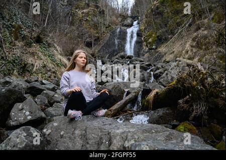 Das Mädchen sitzt auf einem Baum und meditiert in der Nähe des Bergflusses In Abchasien Stockfoto