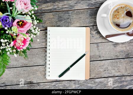Leeres Notizbuch mit Stift, Kaffeetasse und bunten Blumen auf dem Tisch Stockfoto