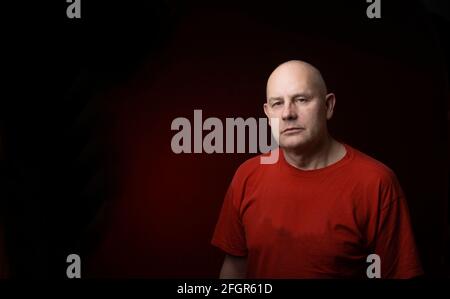 Studio-Porträt eines Mannes mittleren Alters ernstes Gesicht Blick auf die Kamera Isoliert auf dunkelrotem hellem Hintergrund Stockfoto