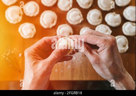 Hände von Senior Mann Kochen und Formen kleine hausgemachte ungekochte Knödel mit Fleisch auf Küchentisch. Nationale traditionelle russische Küche. Tun Sie es Ihre Stockfoto