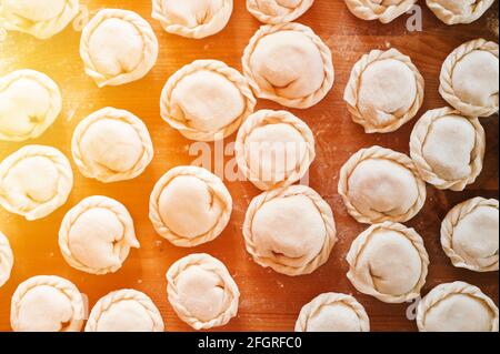 Haufen von kleinen hausgemachten ungekochten Knödel mit Fleisch auf Küchentisch. Nationale traditionelle russische Küche. Tun Sie es selbst. Draufsicht, flach legen Stockfoto