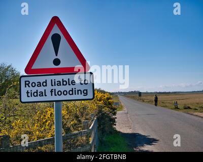 Ein Straßenschild warnt davor, dass die Straße bei Flut überflutet sein könnte. Aufgenommen an einem sonnigen Tag mit blauem Himmel. Stockfoto