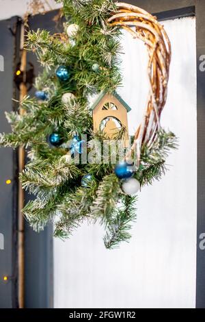 Weihnachtlicher Weidenkranz mit blauen Kugeln und einem kleinen Holzkränz Das Haus hängt an einer Glastür Stockfoto