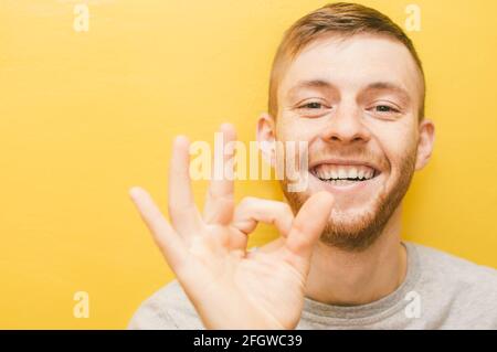 Der junge Mann zeigt mit den Fingern eine gute Geste Lächeln Stockfoto